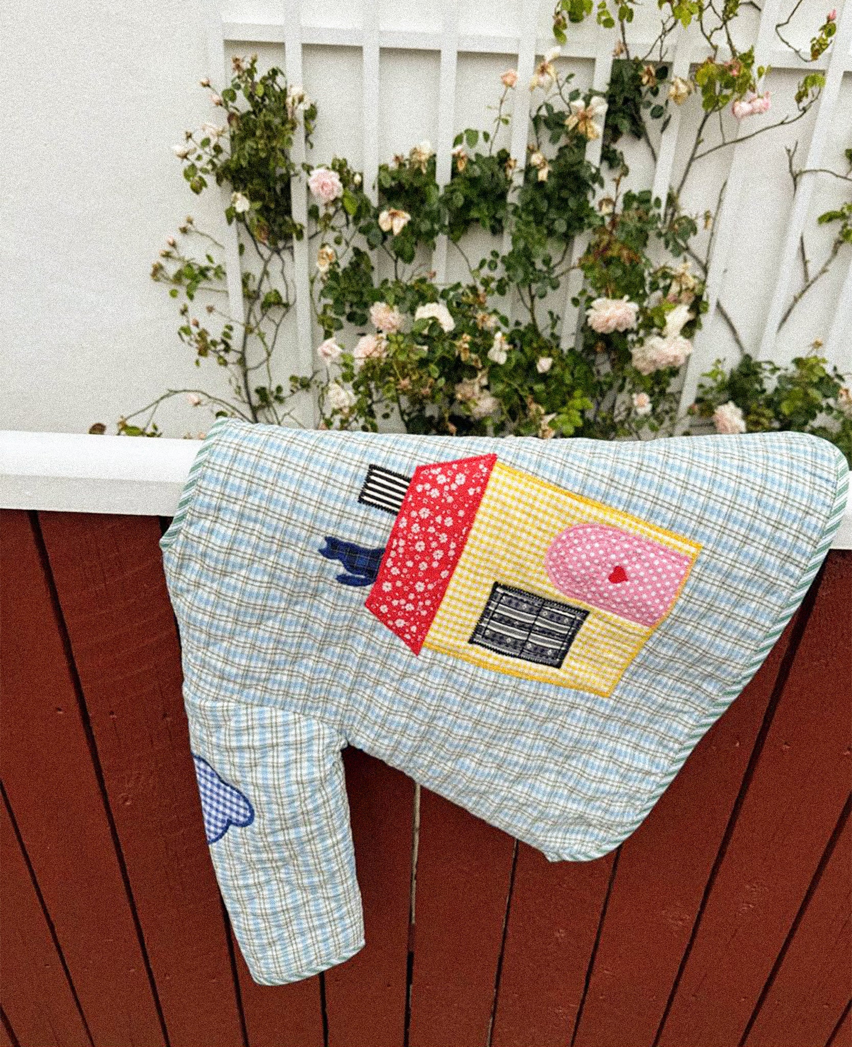 Patchwork quilt with colorful patterns hanging on a wooden fence with flowers in the background from Sissel Edelbo