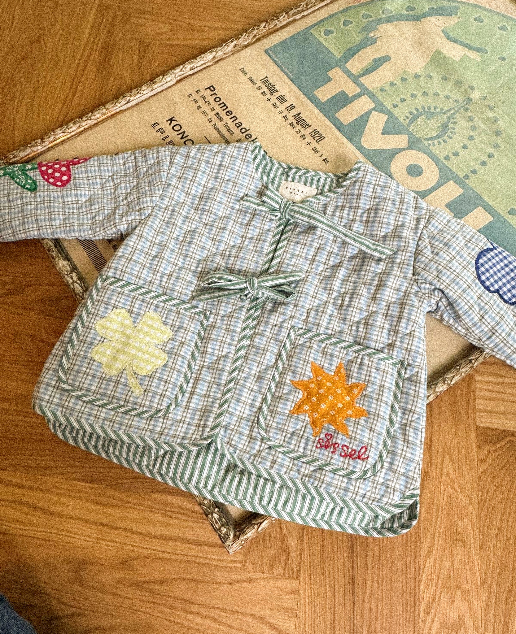 Children's checkered shirt with floral and star designs on a wooden surface from Sissel Edelbo